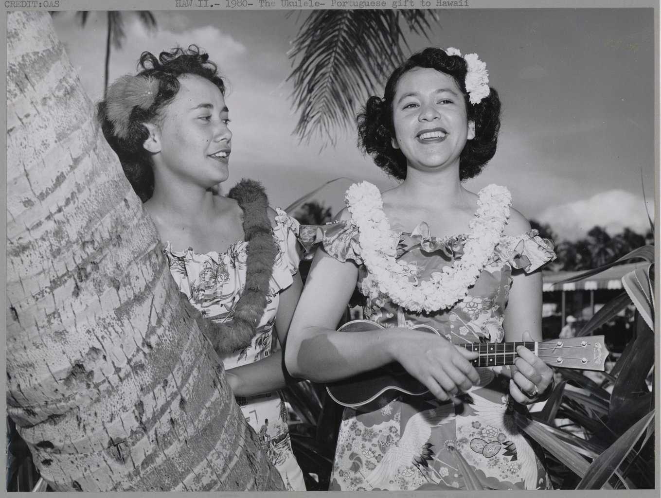 Two young Polynesian women, one playing the ukulele